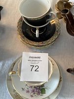Top view of stacked tea cups showing two black tea cups worn and one white floral tea cup in good condition with extra plates and saucers below