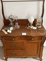 Front view of antique tiger oak wash stand with decorative carved legs and original brass hardware. The top surface holds several vintage items.