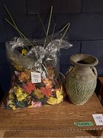 Heavy ceramic vase with patterned surface featuring floral motifs and geometric shapes, placed next to the bag of artificial flowers.