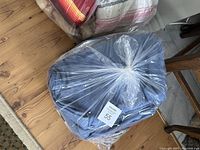 Plastic bags filled with folded bedding items including one prominent blue quilt or blanket and another striped red/orange one, placed on wooden floor.