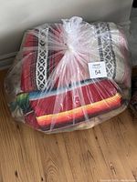 Bagged lot of two Mexican style blankets and one floral comforter wrapped in a clear plastic bag on wood floor.