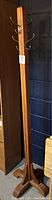 Full view of the tall wooden coat rack stand with metal hooks against a dark wall showing its overall height and four-foot base.