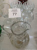 Photo of clear crystal pitcher with pinwheel cut pattern and five assorted clear crystal wine glasses in two sets on a table.