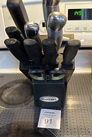 Photo of a black Cuisinart knife block with multiple black-handled kitchen knives and a pair of kitchen scissors.