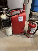 Photo of two fire extinguishers and one water pump extinguisher positioned on a concrete floor in a basement setting, showing visible labels, hoses, pressure gauge, handles, and pump mechanism.