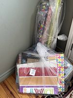 Photo of a bundle of gift wrap rolls and assorted gift bags wrapped in clear plastic bag placed in a corner.