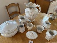 Photo showing entire lot of white porcelain bath ceramics on wooden table, including large pitcher, jugs, covered soap dish.
