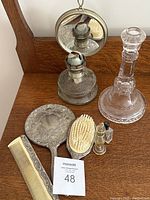 Photo shows the full lot on a wooden surface including antique oil lamp, vintage silver mirror and hairbrush set, glass candlestick holder, small comb, and two small perfume bottles