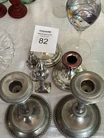 Two-tone silver candlestick holders with salt and pepper shakers and glass oil lamp arranged on tabletop.