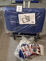 Photo of Pilates Wunda Chair folded with blue padding and foam handles, accompanied by several workout DVDs and an exercise instructions booklet on top.