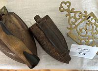 Close-up view of two antique irons, one wooden handle, one metal handle, and brass stand.