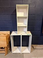 Tall white shelving unit placed on top of shorter white shelving unit against a dark wall, showing three shelves on the taller unit and two large compartments in the shorter unit. Visible dirt and dust indicating need for cleaning.