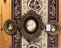 Full view of the three-piece vintage portrait set on decorative rug showing ornate plastic frames with velvet surrounds and convex glass
