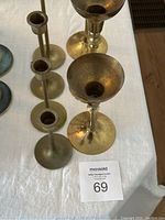Top down view of six vintage brass candlesticks on white tablecloth, varying height and design