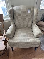 Full view of the upholstered wing back chair showing the diamond patterned fabric, rolled arms, wooden legs with caster wheels