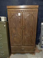 Full front view of vintage wood armoire showing carved doors and wood grain finish
