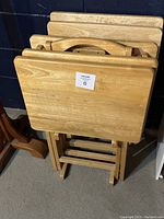 Wooden small folding tables stacked together in a wooden stand with smooth rectangular tabletops.