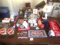 Full view of lot contents including Coca-Cola branded dispensers, jars, flatware, clocks, blanket, and various decor.