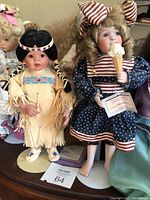 Group of 16 ceramic dolls on stands, showing front row with Native American dress doll and polka dot dress doll holding ice cream cone