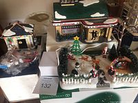 Overview of multiple Snow Village buildings and accessories displayed on a table with snow-covered rooftops and small figurines in a winter holiday setting.