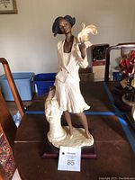 Full figurine showing the entire ceramic statue of an African woman holding a feather, standing on a base.