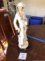 Full view of the 18 inch tall statue showing the woman in cream-colored dress with fur trim and umbrella, on a decorative base with manufacturer plaque.