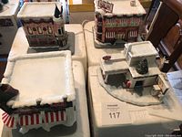 Four miniature buildings on a table: a diner, pharmacy, market, and gas station with snow details.