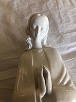 Front top view of the white ceramic Madonna figure showing face and upper body with hands clasped in prayer.