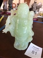 Full front view of pale green jade standing Buddha statue on a table with background figurines.