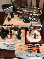 Overview photo of all four collectible miniature buildings and accessories grouped together on a table, showing the diner, Christmas shop, winter scene, and tree lot accessory.