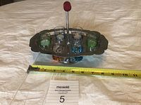 Front angled view showing six tinted shot glasses sitting in oval metal stand with measuring tape revealing overall length and width approximately 9x6 inches.