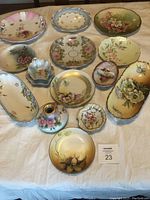 Overview of vintage hand painted china plates and dishes laid out on cloth, showing various floral designs and shapes.