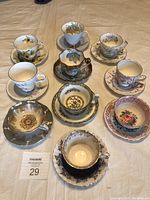 Full view of ten vintage teacup and saucer sets arranged on a table displaying different floral and decorative styles.