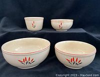 Four vintage ceramic Cambridge Universal bowls displayed on black cloth backdrop. Front two bowls are larger, rear two are smaller, all decorated with red and black floral motif and red rim line.