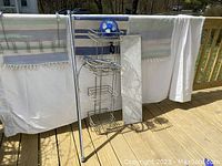 Photo showing the chrome shower curtain rod, brushed corner rack, marble slab, and small blue fan arranged on an outdoor deck.