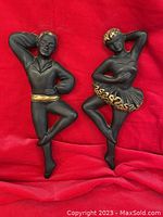 Pair of black plaster ballet dancer plaques with gilt accents on red fabric background, showing full figures and wire hooks