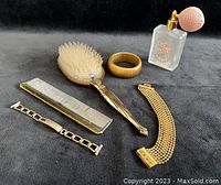 Full vanity set including atomizer, hairbrush, comb, and three gold-washed bracelets on dark background