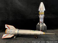 Side view of silver Holdraketa friction rocket ship lying horizontally next to silver Boston Federal Bank rocket coin bank standing vertically