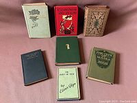 Seven vintage books arranged on a pink surface, covers visible showing a variety of colors and bindings