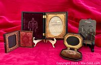 Photo showing three antique daguerreotype cases including two black thermoplastic hinged cases and one wood tooled leather case alongside a tintype photo of two stern men.