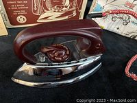 Close-up of the travel iron showing chrome base, dark brown handle, and temperature dial.