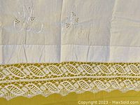 Close-up showing embroidered floral initials 'M' and 'A' with delicate tatted edges on a white linen bedsheet