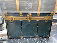 Front view of antique steamer trunk showing blue panels with black edges and brass hardware, including central lock plate without key.