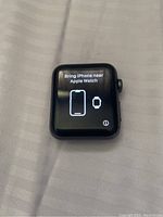 Front display of Apple Watch showing pairing instructions in English to bring iPhone near Apple Watch.