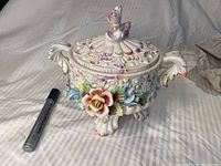 View of the candy bowl with lid in profile, showing floral decoration and handle detail with major flower embellishment.