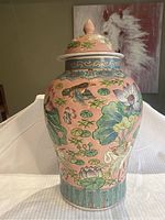 Front view of ceramic ginger jar showing detailed crane and lotus flower painting on pink background, with a portion of a white cloth under it.