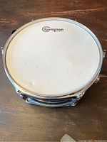 Top view of snare drum showing white Gammon drumhead with small perforations and dents, black drum body, and metallic tuning rods