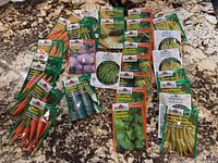 Full layout of various seed packets on countertop showing carrot, cucumber, green beans, herbs and summer squash seeds.