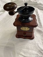Manual coffee grinder with wood base and metal top with hand crank on a white fabric surface.
