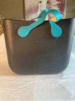 Front view of the black O bag with turquoise handles and embossed logo.